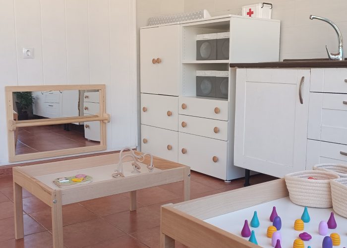 Espejo Montessori Zona con espejo Montessori, mesas de experimentación y armario con material diverso.