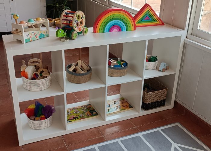 Zona de juegos Estantería con materiales Montessori y Waldorf: cesto de los tesoros, telas, puzles, instrumentos musicales, coches, piezas de madera para construcciones...